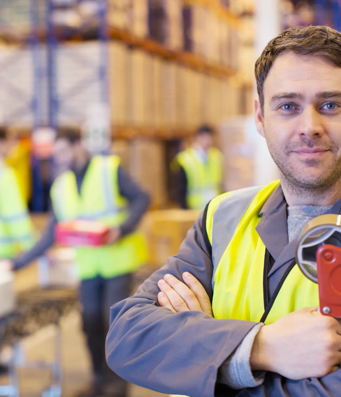 Warehouse worker smiling, on a background of warehouse racks and coworkers unloading boxes onto a conveyor belt