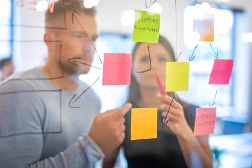 Team working on a transparent board, writing notes on post-its during workshop