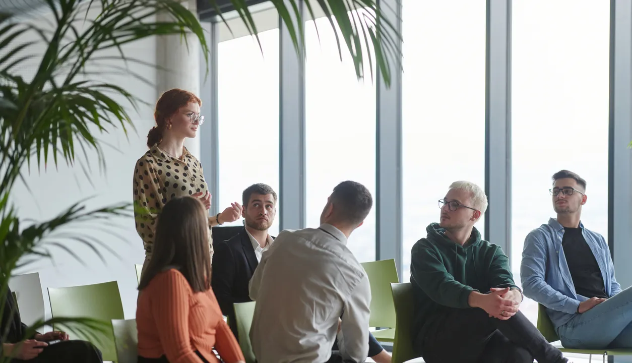 A diverse group of business professionals sits attentively in a modern office, actively participating in a training session led by an instructor, focusing on the latest technological advancements in the business world. - Stockbeeld